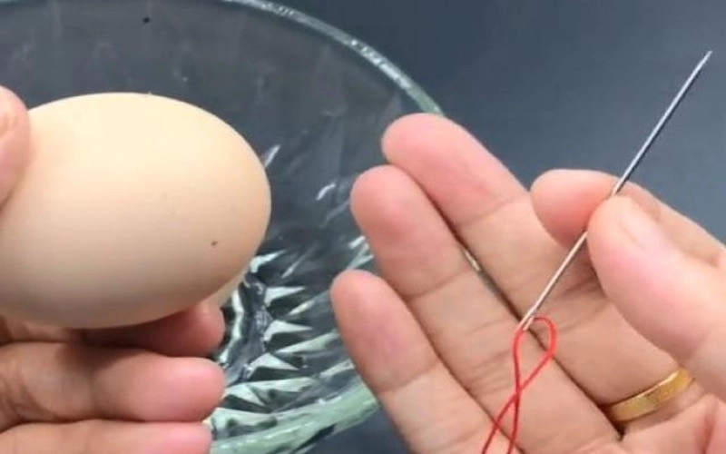 Dùng một cây kim và một sợi chỉ đỏ xâu xuyên qua quả trứng gà, sao cho quả trứng gà nằm ở giữa.